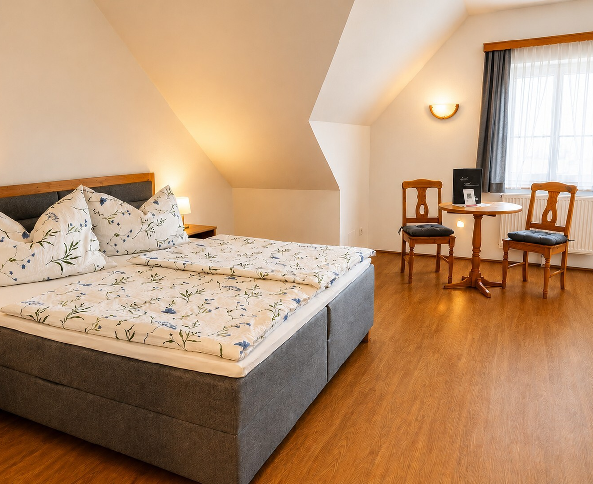 Doppelzimmer mit einem Doppelbett, einem kleinen Tisch mit zwei Stühlen und einem Fenster.
