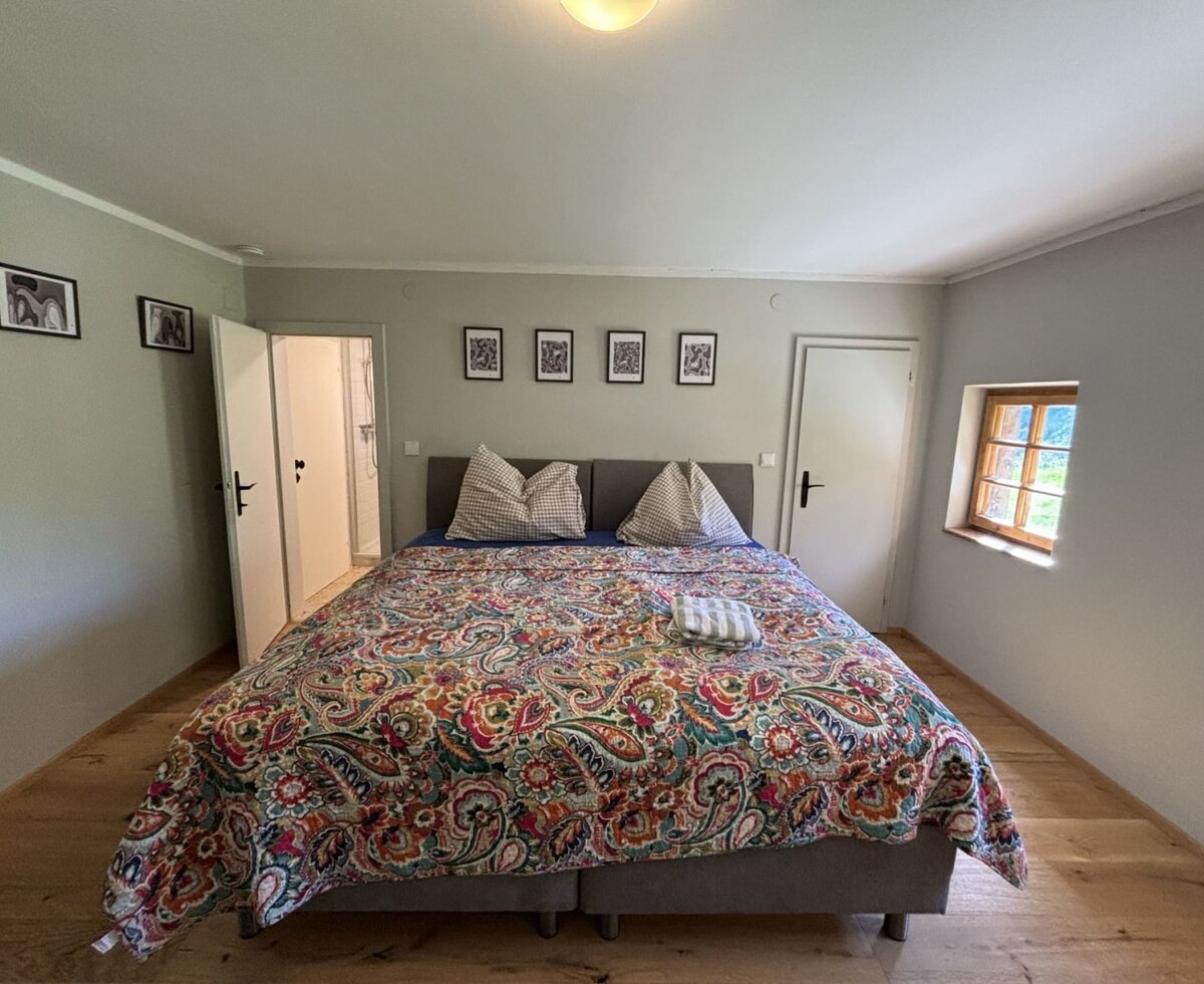 Doppelzimmer mit Doppelbett, Holzboden und einem kleinen Holzfenster.