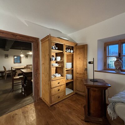 Im kleinen Wohnzimmer mit Ausziehcouch: Holzschrank mit Geschirr, mit Zugang zum Essbereich und Blick auf die Umgebung durch das Fenster.