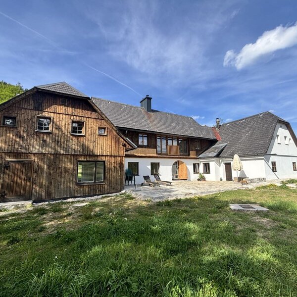 Außenansicht mit Holzfassade, weißem Putz und einer Terrasse mit Liegestühlen.