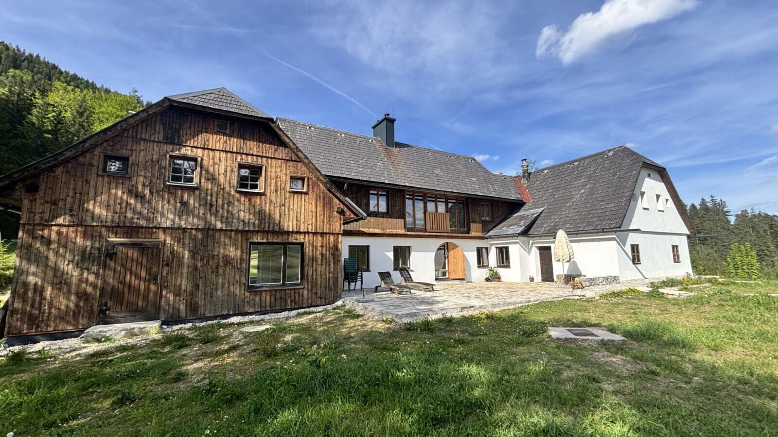 Außenansicht mit Holzfassade, weißem Putz und einer Terrasse mit Liegestühlen.