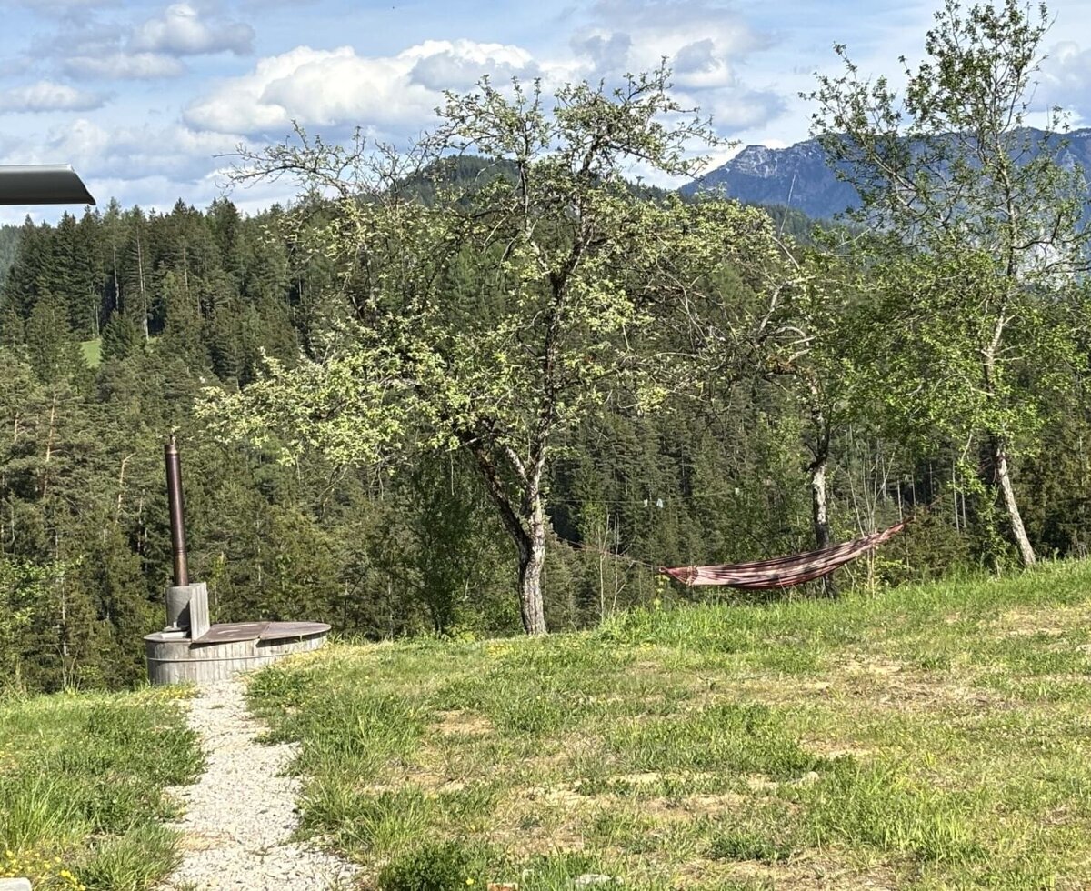 Der Außenbereich mit einem Holzbadezuber, einer Hängematte und Blick auf Wald und Berge.
