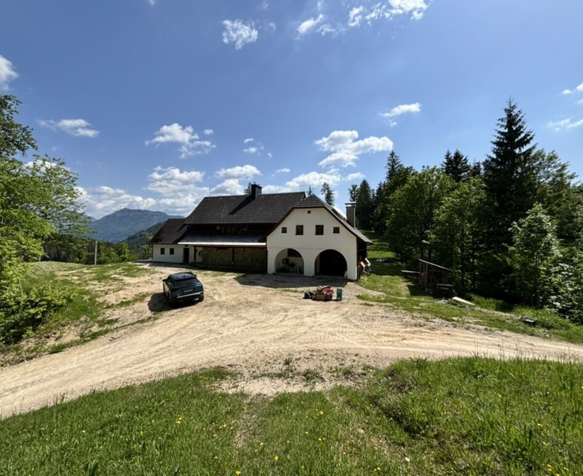 Außenansicht des Amerikaners mit einem großen Schotterparkplatz, umgeben von Wiesen, Bäumen und Bergen im Hintergrund.