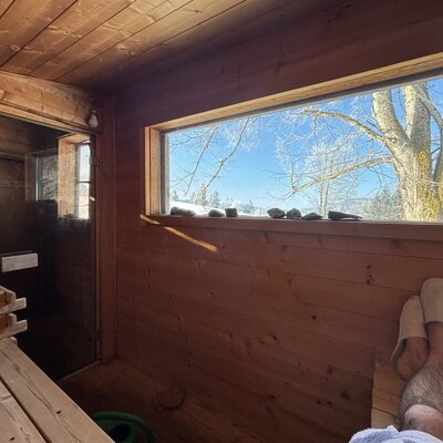 Sauna mit Blick iun den Sonnenuntergang im Aussenbereich des Ferienhauses Hinterbreiteneben  mit Holzinterieur und großem Fenster mit Blick auf die verschneite Landschaft.