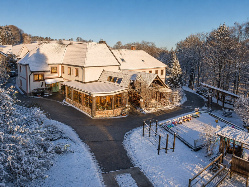 Der einladende Bauernhof im idyllischen Wintergewand mit schneebedecktem Außenspielplatz und sonnigem Innenhof.