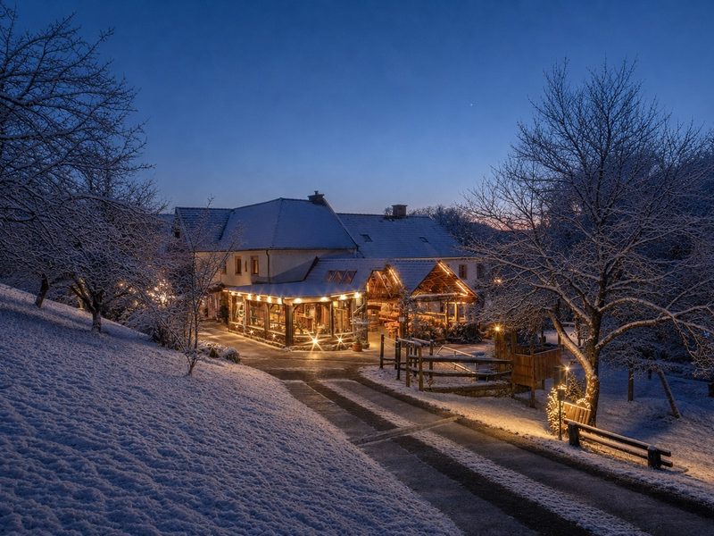 Der stimmungsvoll beleuchtete Bauernhof eingebettet in eine verschneite Winterlandschaft in der Abenddämmerung.