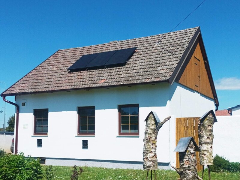 Das Ferienhaus mit Solarmodulen auf dem Dach und einem grünen Gartenbereich unter blauem Himmel.