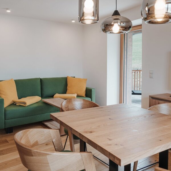 Einladender Wohnbereich des Landhofs mit einem massiven Holztisch, gemütlichem grünem Sofa und modernem Fernseher.