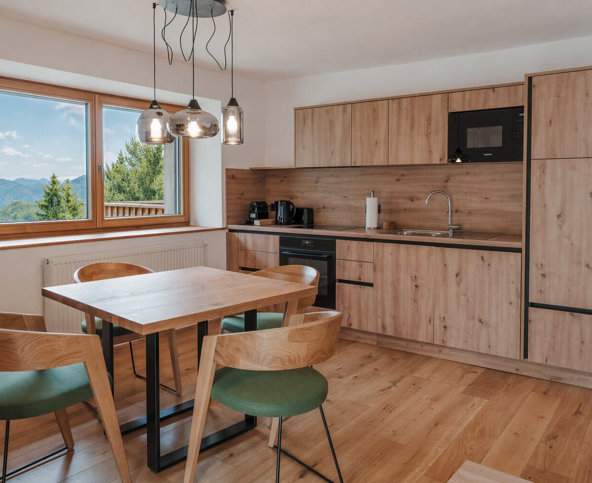 Die einladende Wohnküche des Landhofs verfügt über eine moderne Küchenzeile aus Holz, einen gemütlichen Essbereich und einen schönen Ausblick auf die Natur.