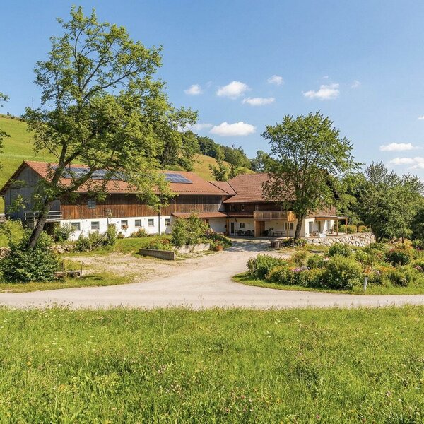 Der einladende Landhof, umgeben von weitläufigen grünen Wiesen unter blauem Himmel.