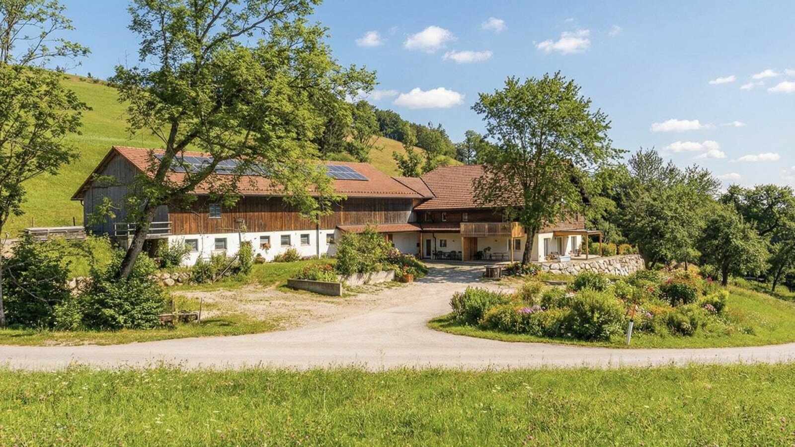 Der einladende Landhof, umgeben von weitläufigen grünen Wiesen unter blauem Himmel.