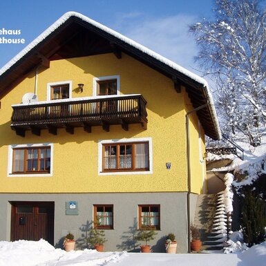 Außenansicht des Gästehauses mit gelber Fassade, Holzbalkon und Außentreppe im Winter.