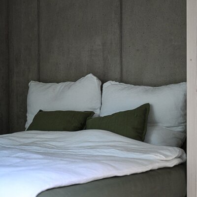 Ein einladendes Bett mit gemütlichen Kissen vor einer modernen Sichtbetonwand.