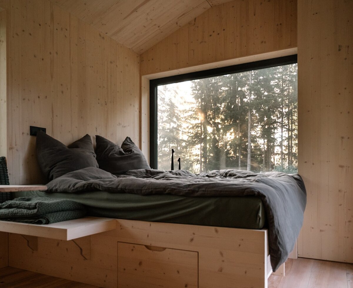 Ein gemütliches Schlafzimmer mit warmen Holzwänden, einem einladenden Bett und einem großen Panoramafenster mit Blick in den Wald.