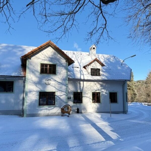 Außenansicht des Bauernhofs im Winter, mit schneebedecktem Dach und verschneiter Umgebung.