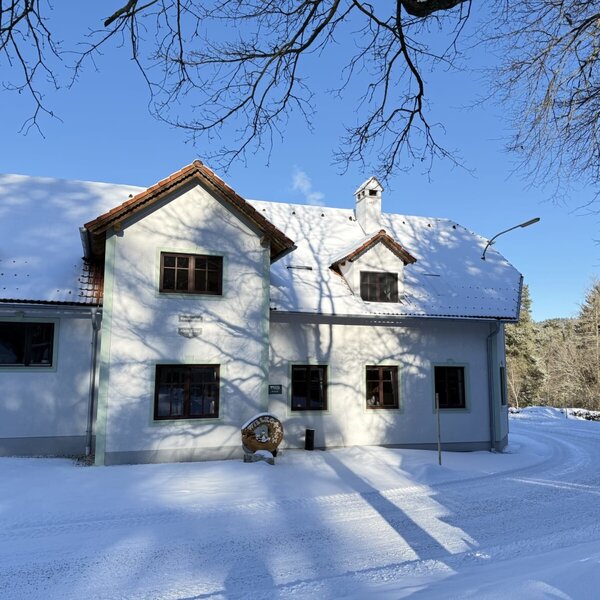 Außenansicht des Bauernhofs im Winter, mit schneebedecktem Dach und Umgebung unter blauem Himmel.