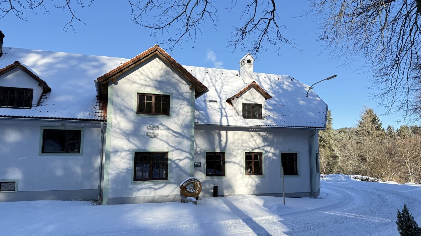 Außenansicht des Bauernhofs im Winter, mit schneebedecktem Dach und Umgebung unter blauem Himmel.