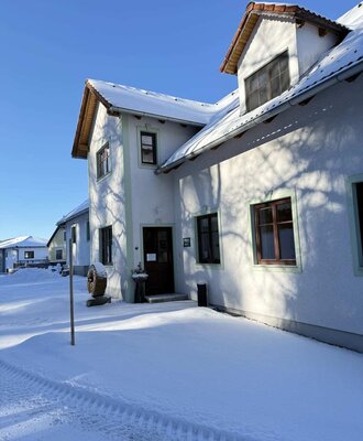 Außenansicht des Bauernhofs im Winter, mit Schnee auf dem Dach und dem Eingangsbereich.