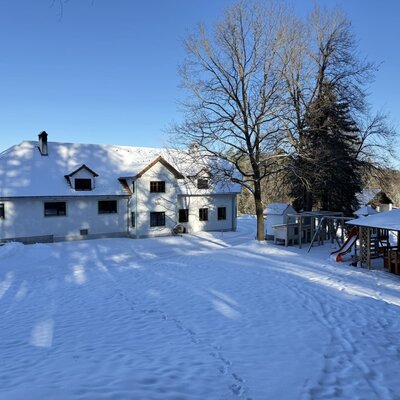 Der Bauernhof im Winter mit schneebedecktem Garten, Spielplatz und Pavillon.