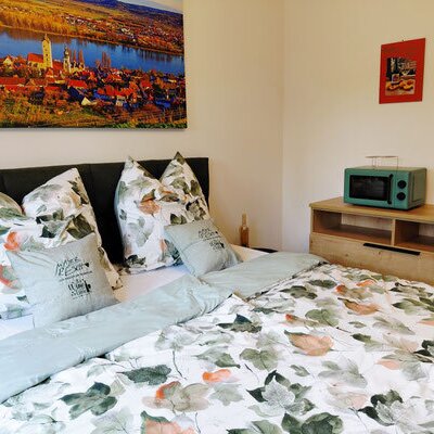 Ein gemütliches Doppelbett mit floraler Bettwäsche, einer Holzkommode und farbenfroher Wanddekoration im Winzerhof.