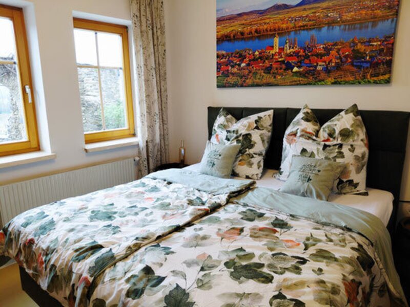 Ein gemütliches Doppelzimmer des Winzerhofes mit einem einladenden Bett in frischem floralem Design und hellem Tageslicht.