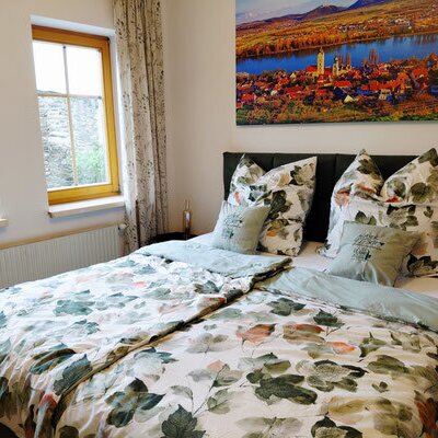Ein gemütliches Doppelzimmer des Winzerhofes mit einem einladenden Bett in frischem floralem Design und hellem Tageslicht.