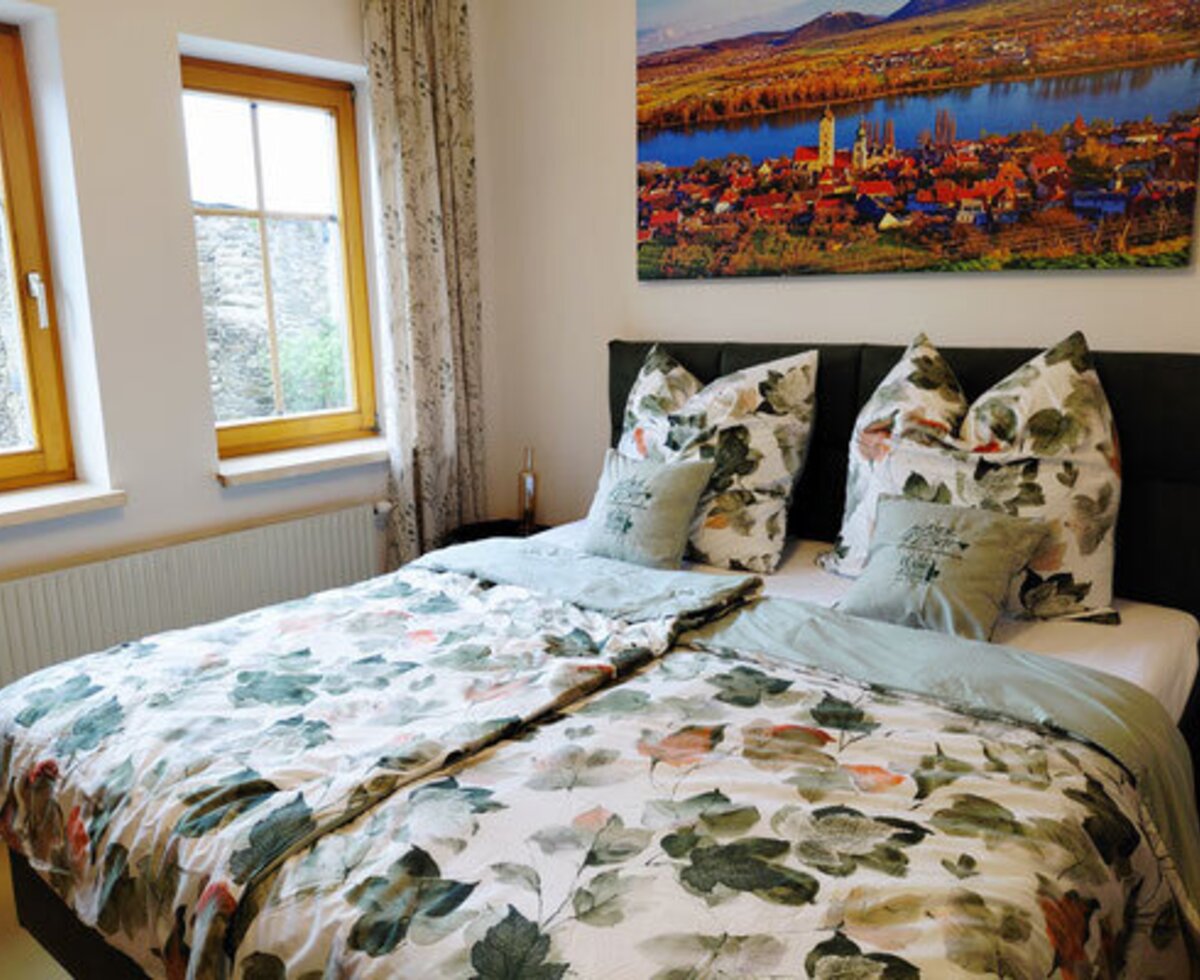 Ein gemütliches Doppelzimmer des Winzerhofes mit einem einladenden Bett in frischem floralem Design und hellem Tageslicht.