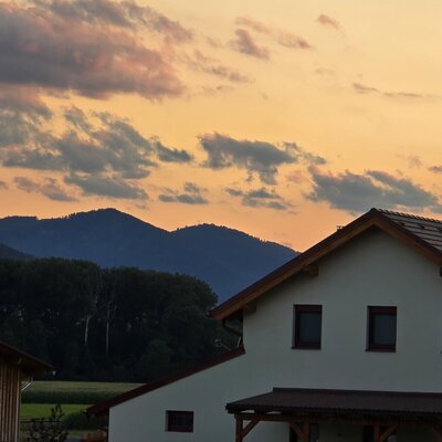 Blick auf das Gebäude des Bauernhofs mit Ziegeldach und die umliegende Berglandschaft bei Sonnenuntergang.