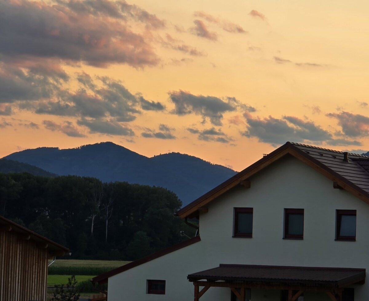 Blick auf das Gebäude des Bauernhofs mit Ziegeldach und die umliegende Berglandschaft bei Sonnenuntergang.