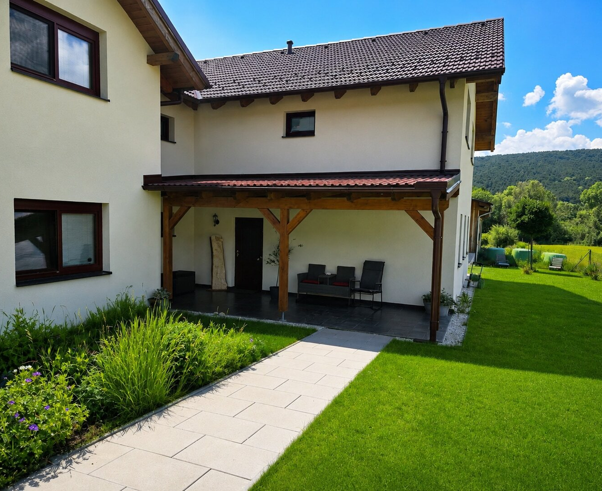 Außenansicht des Bauernhofs mit überdachter Terrasse, Sitzgelegenheiten, Rasenfläche und Blick auf die umliegende Hügellandschaft.