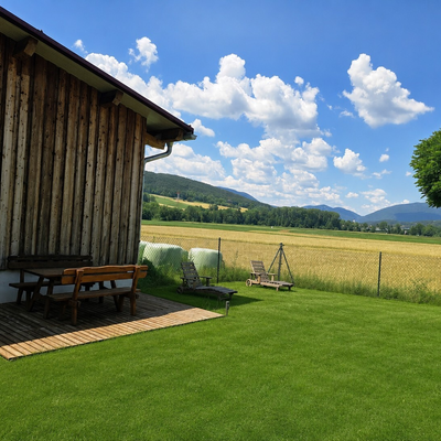 Der Außenbereich des Bauernhofs mit einer Holzterrasse, Picknicktisch, Liegestühlen und Blick auf die umliegenden Felder und Berge.