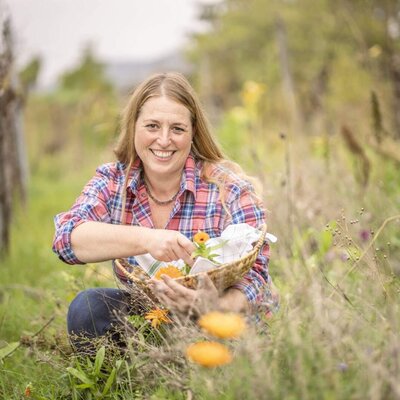 Frau Stefanie sammelt Ringelblumen in einem Korb im Naturgarten.