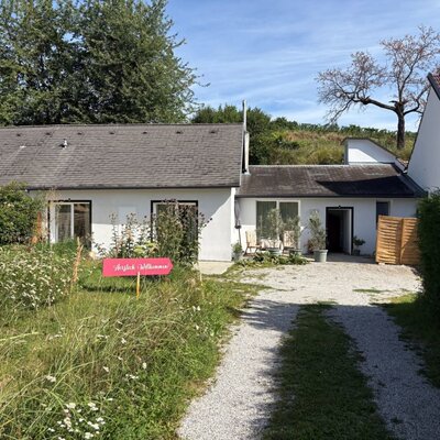 Einfahrt mit einem Willkommensschild, einem kleinen Garten und einer Terrasse mit Sitzgelegenheiten.