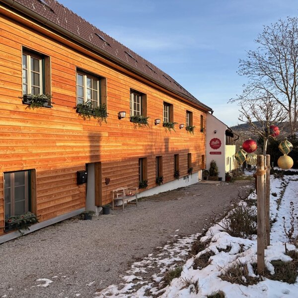 Außenansicht mit Holzfassade, Kiesweg und verschneitem Gartenbereich.