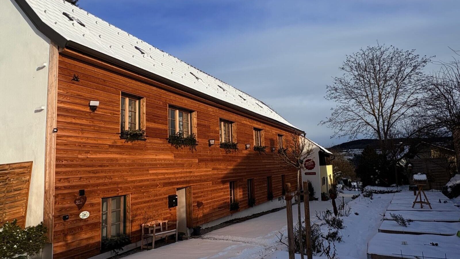 Außenansicht Landhaus mit Holzfassade und schneebedecktem Dach im Winter.