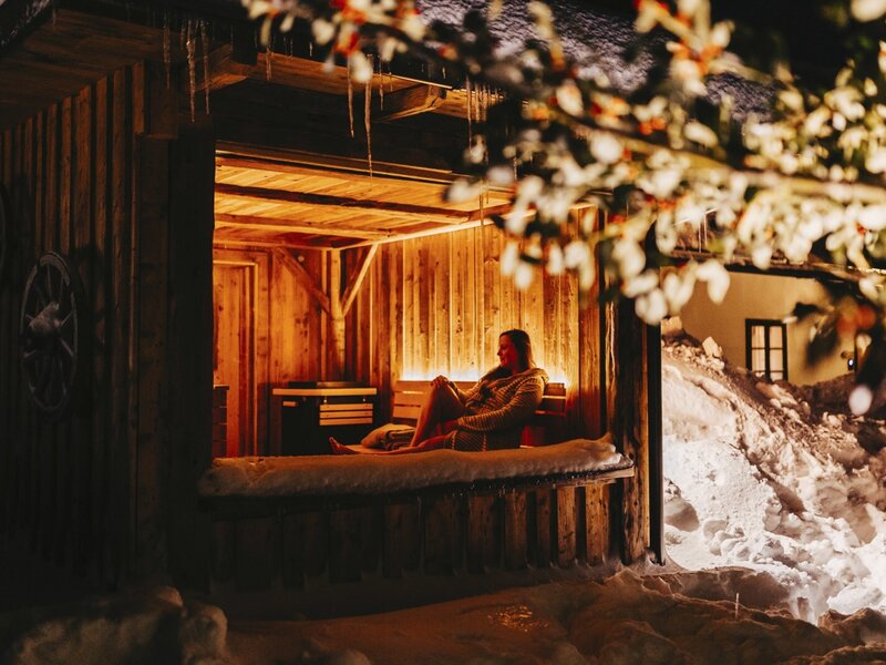 Holzverkleideter, beleuchteter Ruhebereich mit Sitzgelegenheiten für Gäste des Ferienhauses, umgeben von Schnee.