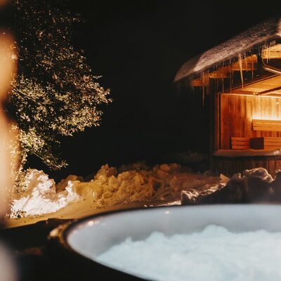 Außen-Whirlpool und Sauna des Ferienhauses, umgeben von Schnee bei Nacht.