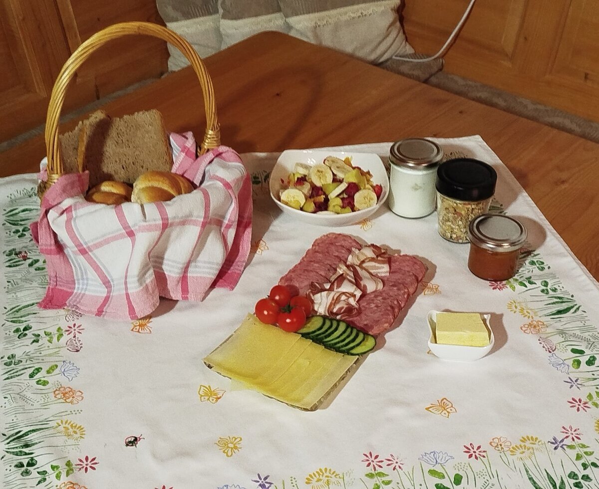 Frühstück auf dem Bauernhof mit Brot, Brötchen, Käse, Wurst, Obstsalat und Marmelade.