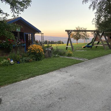 Der Garten des Bauernhofs mit Kinderspielplatz, Schaukel, Rutsche, einer kleinen Holzhütte und Bergblick.