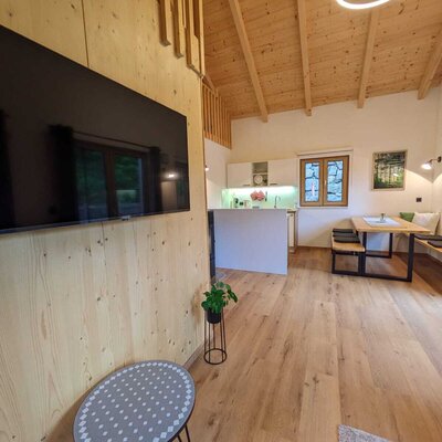 Wohnbereich des Ferienhauses mit großem Fernseher, offener Küche und Essbereich mit Holztisch und Sitzbänken.
