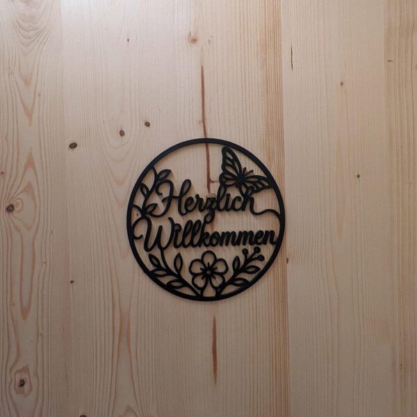 Willkommensschild mit Schmetterling und Blumenmotiv an einer Holzwand des Ferienhauses .