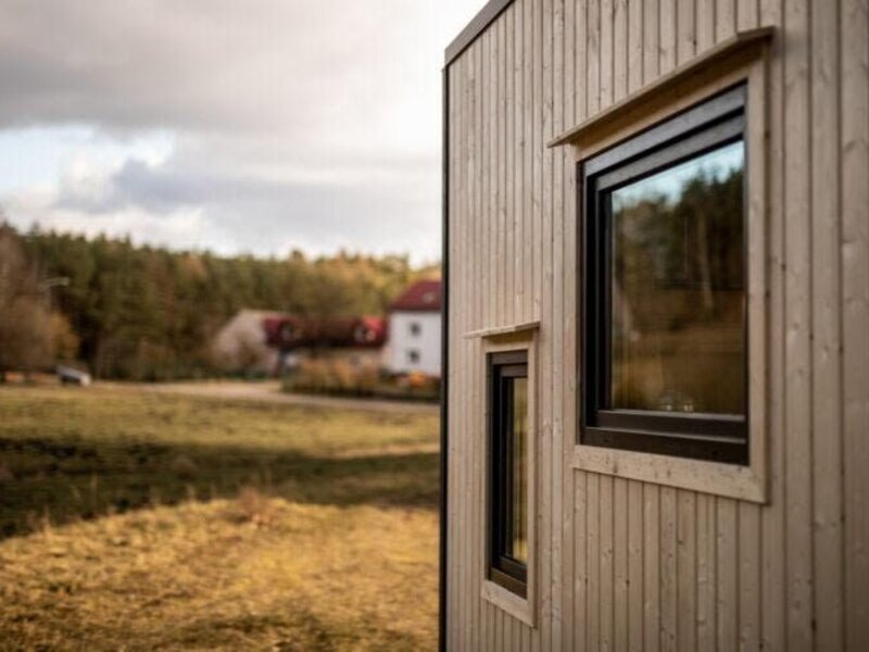 Die Holzfassade des Tiny Haus mit Fenstern und Blick auf die umliegende Natur.