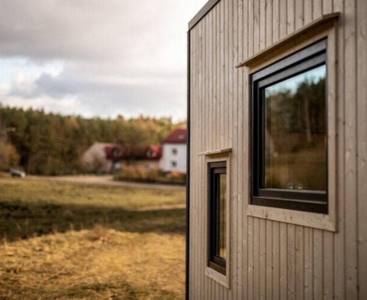 Die Holzfassade des Tiny Haus mit Fenstern und Blick auf die umliegende Natur.