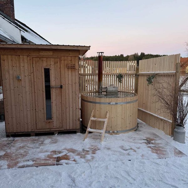 Außensauna und ein hölzerner Badezuber im Schnee am Hof.