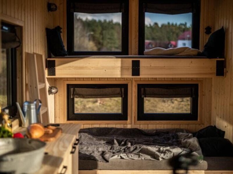 Schlafbereich im Tiny Haus mit zwei Schlafebenen, Holzinterieur und einer kleinen Küchenzeile.
