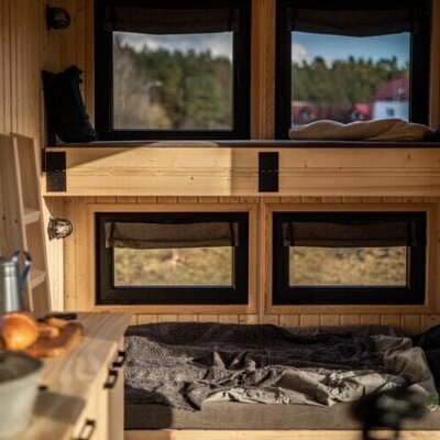 Schlafbereich im Tiny Haus mit zwei Schlafebenen, Holzinterieur und einer kleinen Küchenzeile.
