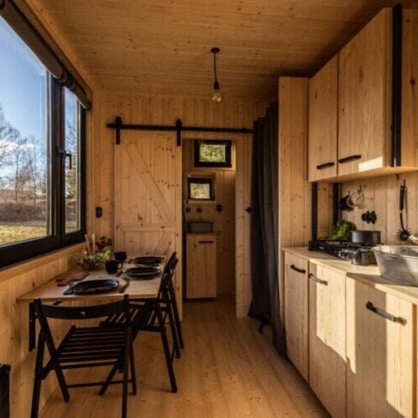 Küche und Essbereich des Tiny Haus mit Holzausstattung, einem Esstisch für vier Personen und einer Küchenzeile mit Herd und Spüle.