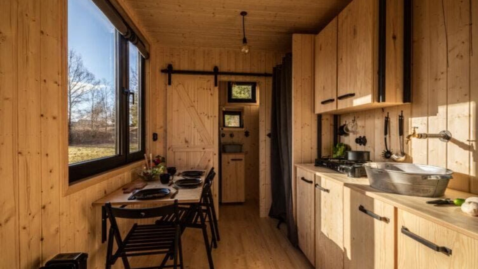 Küche und Essbereich des Tiny Haus mit Holzausstattung, einem Esstisch für vier Personen und einer Küchenzeile mit Herd und Spüle.