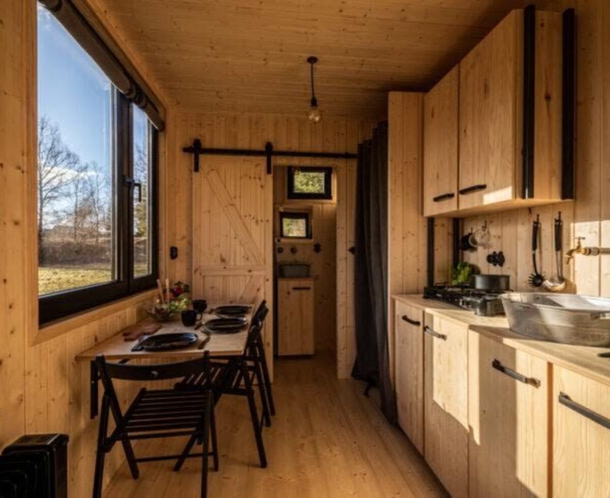 Küche und Essbereich des Tiny Haus mit Holzausstattung, einem Esstisch für vier Personen und einer Küchenzeile mit Herd und Spüle.