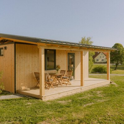Ein gemütliches Holzhaus des Bauernhofs mit einer überdachten Terrasse und einer einladenden Sitzgruppe im Grünen.